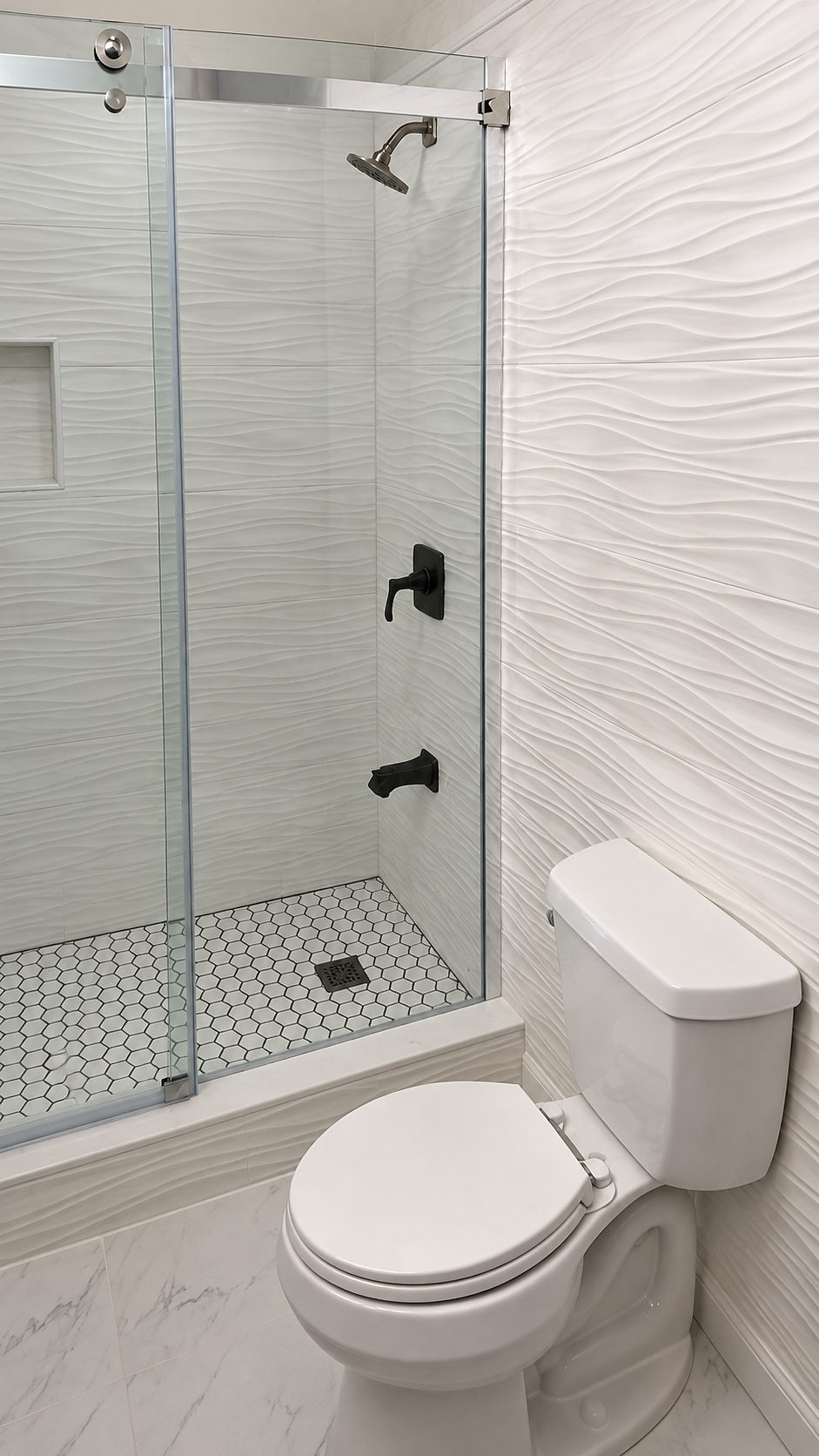 Bathroom with a glass shower door, white wave-textured wall tile, black fixtures and a hex-tile floor