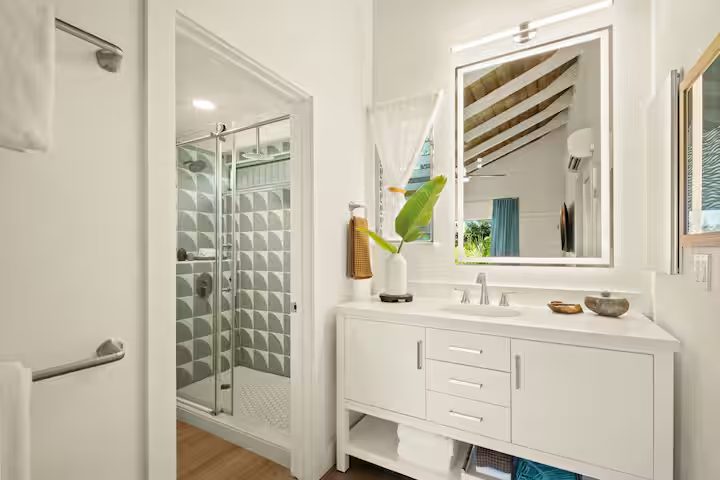 Bathroom with a walk-in shower in green geometric tile, a white vanity and a large mirror