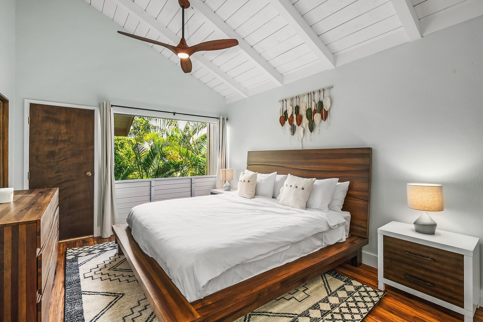 Bedroom with a vaulted white ceiling, wood headboard and a window to the palms