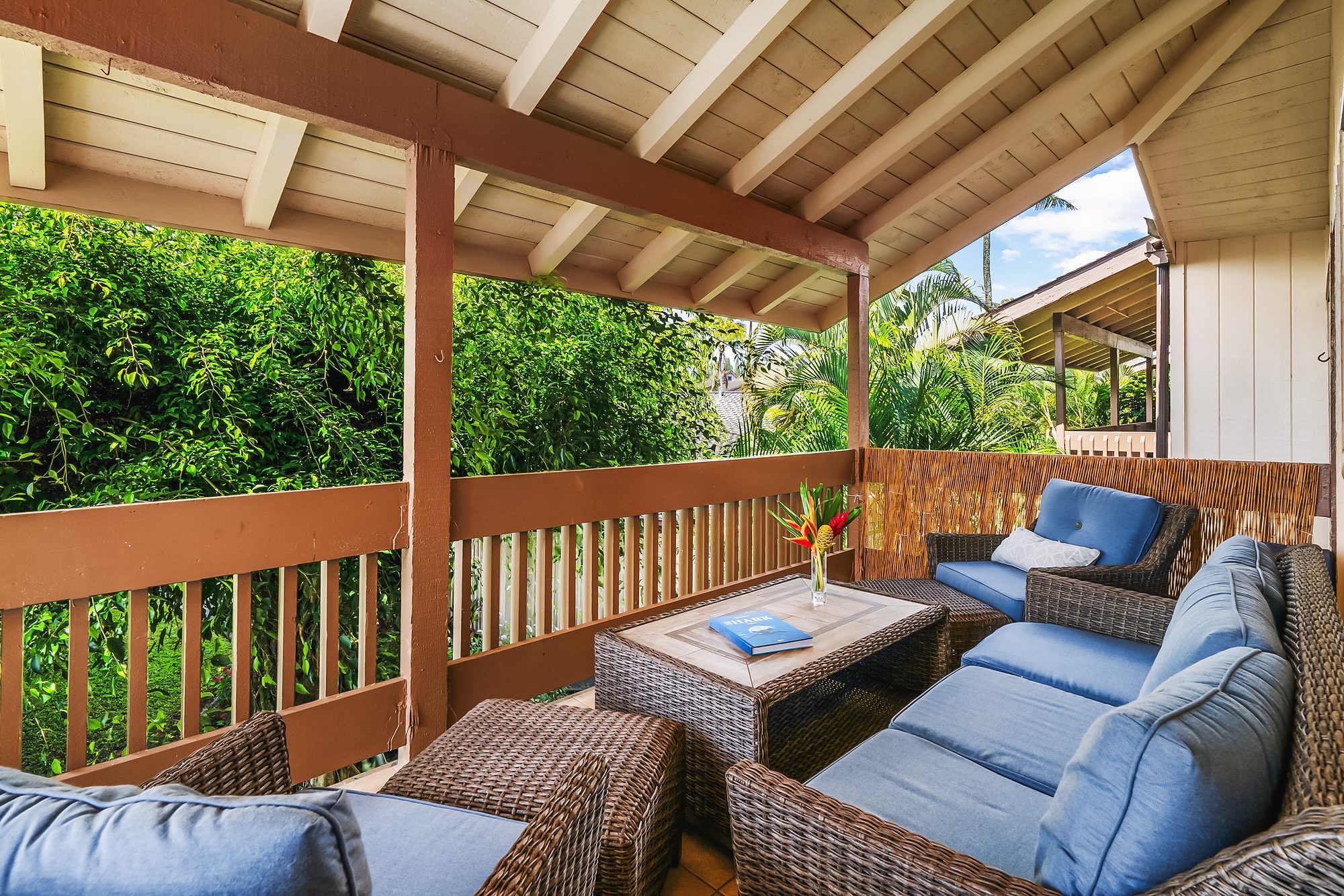 Covered lanai with a blue sectional sofa, wood railing and garden beyond