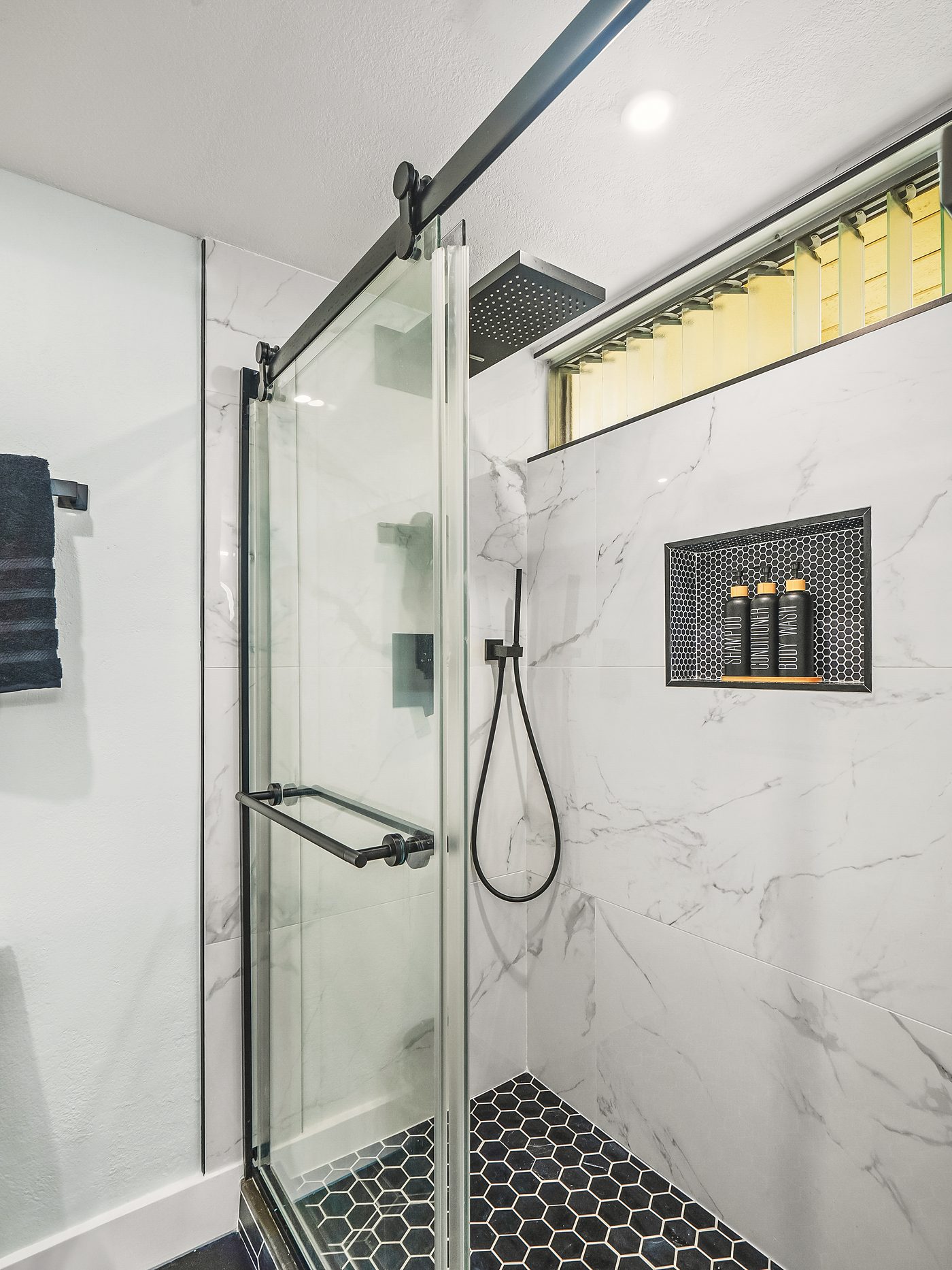 Walk-in glass shower in large-format marble tile with a black hex floor