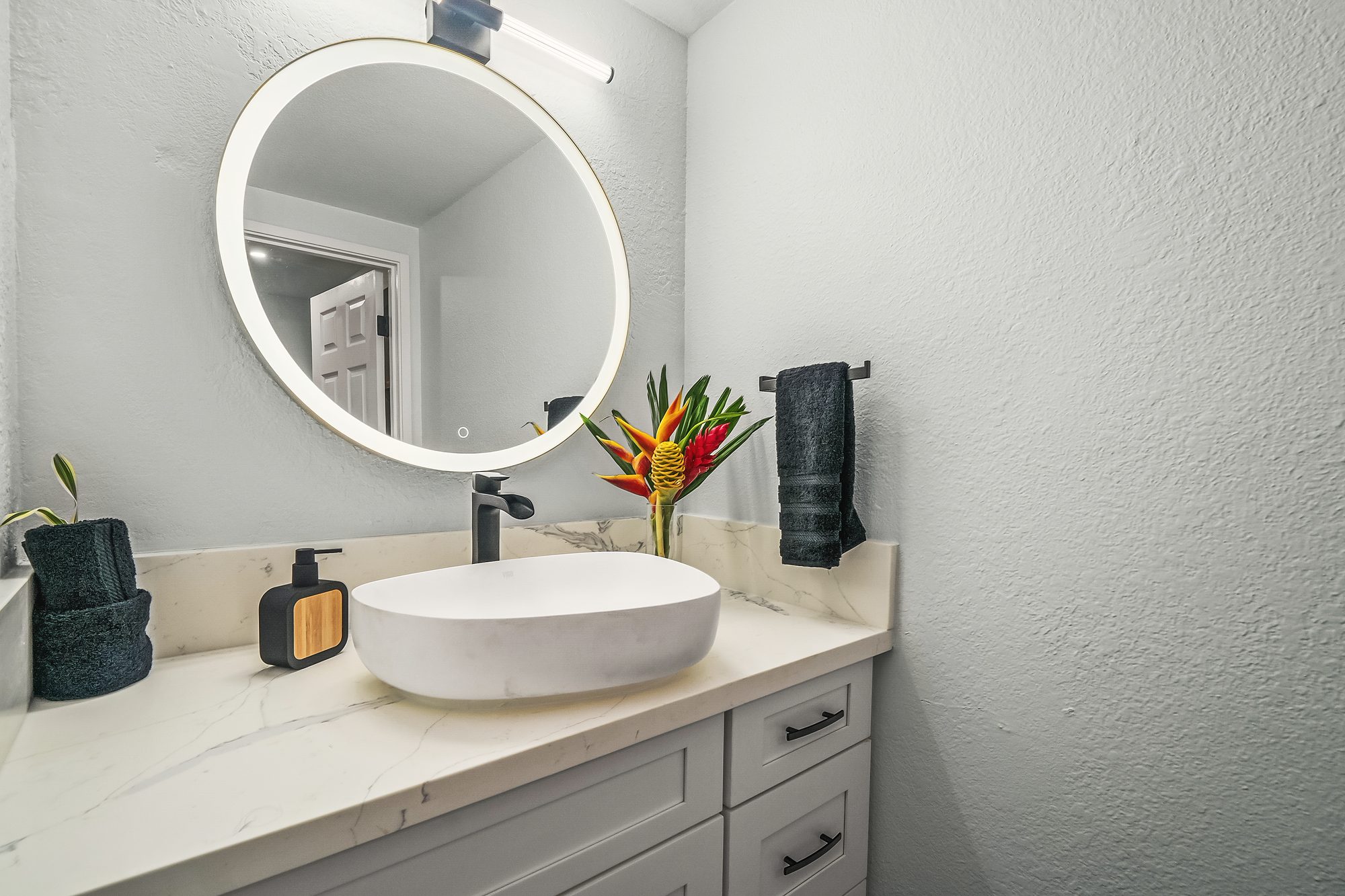 Vanity with a vessel sink and a round mirror beside the kitchenette