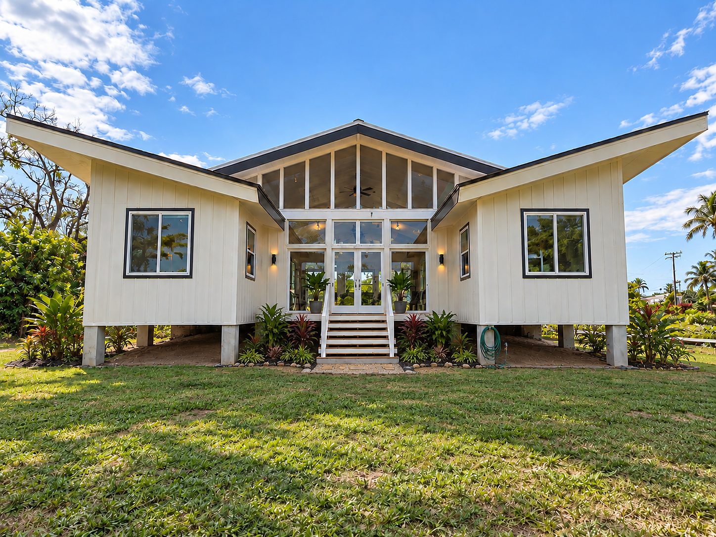 The finished Kapa‘a home from the front lawn: white walls, glass gable, lifted roof
