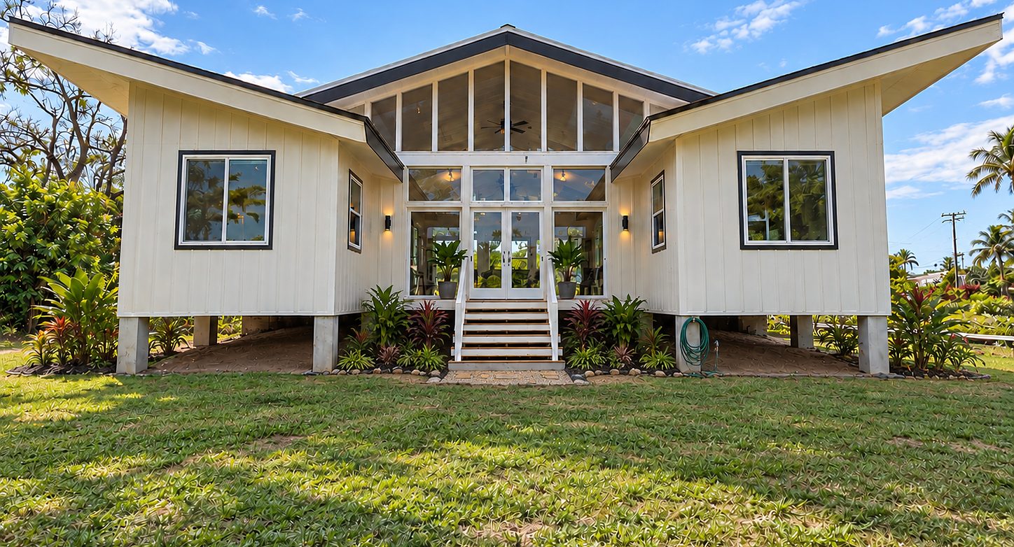 Finished custom home in Kapa‘a at golden hour: lifted roof, glass gable, lanai and steps to the lawn