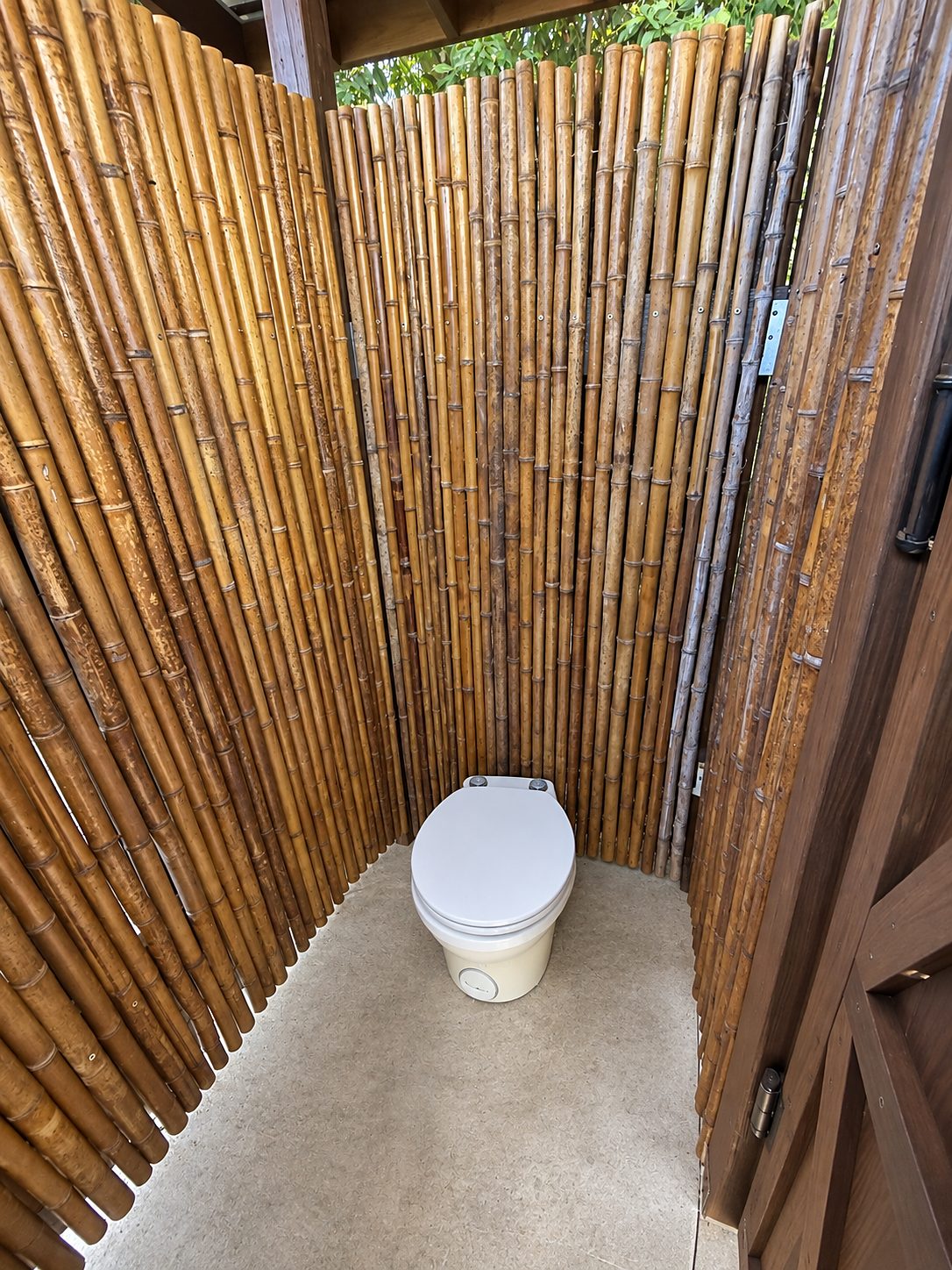 Outdoor bathroom with bamboo walls and a toilet on a concrete floor