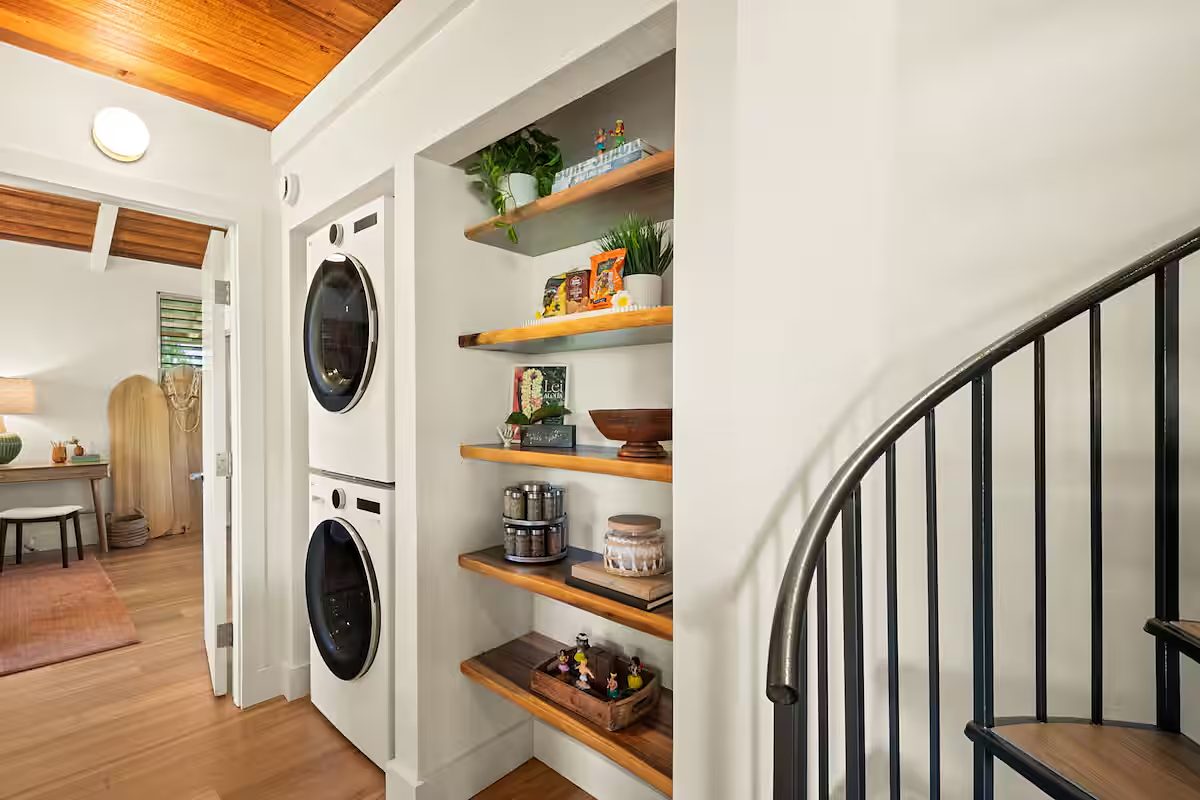 Floating wood shelves beside the black spiral stair, stacked washer and dryer behind