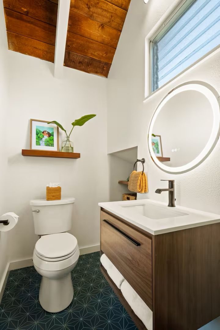 Half bath under a wood ceiling with a round mirror, walnut floating vanity and blue geometric floor tile