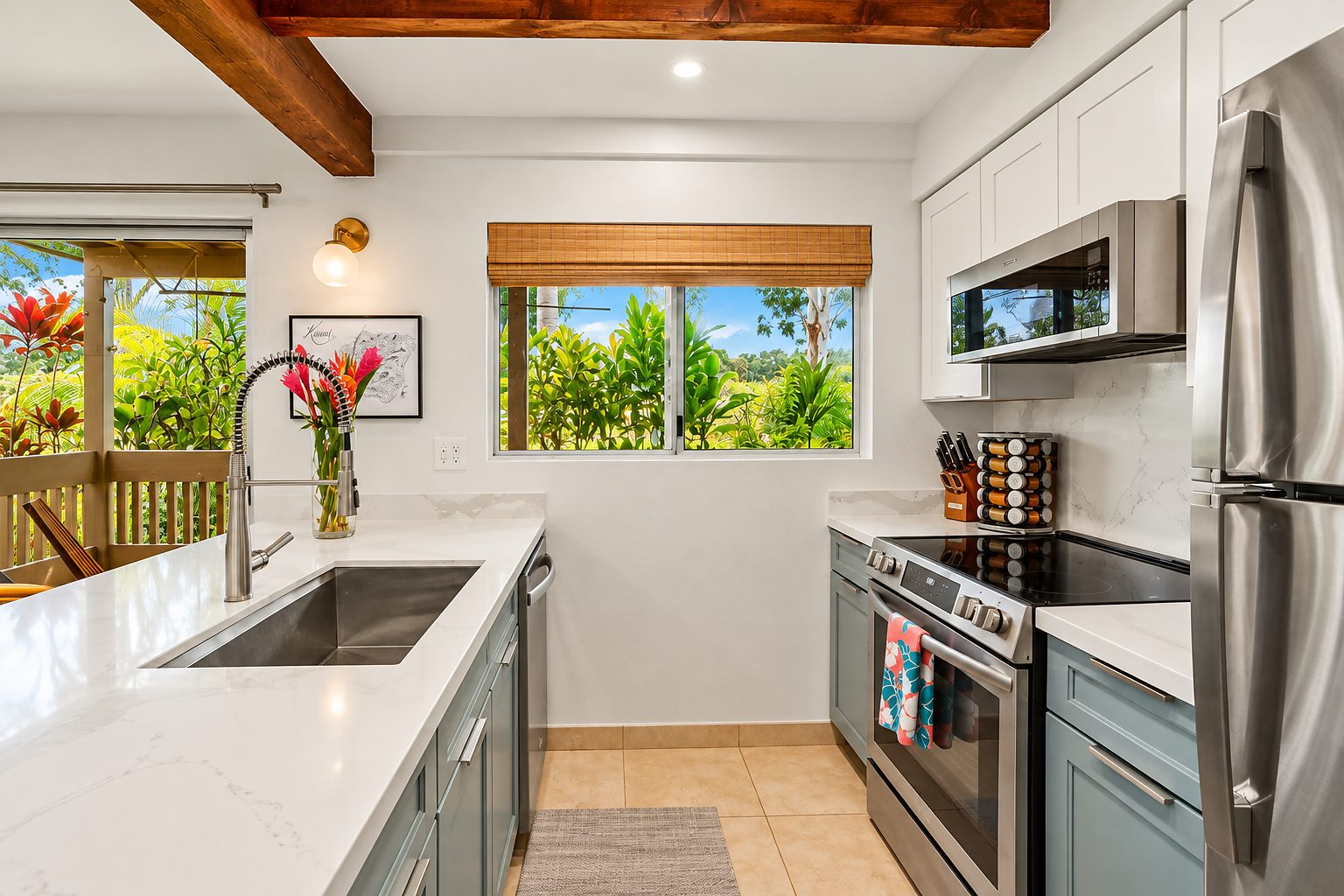 Kitchen with exposed beams, white upper cabinets, teal lowers and red flowers in the window