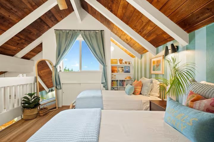 Sleeping loft under the wood ceiling with twin beds, a white railing and an arched mirror