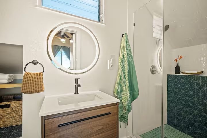 Bath with a round mirror, walnut vanity and green tile