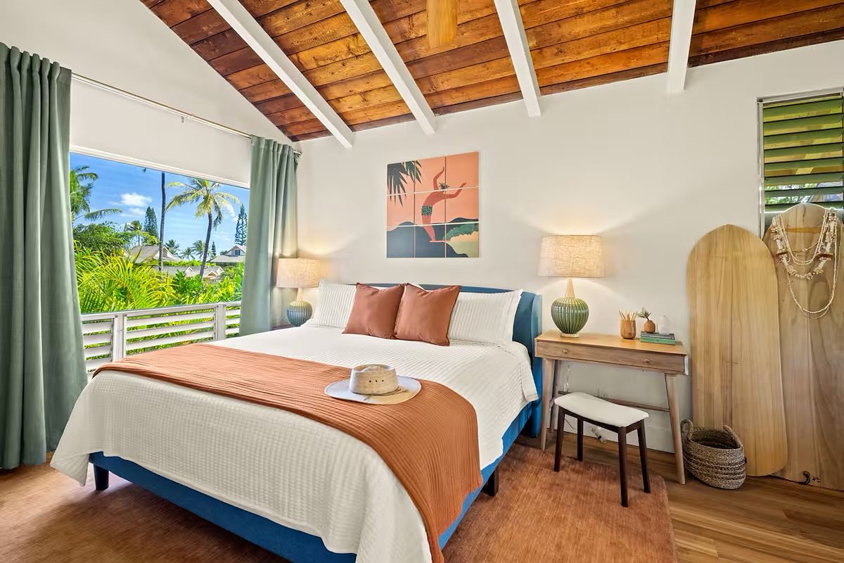 Bedroom under the wood ceiling with teal curtains and a window to the palms
