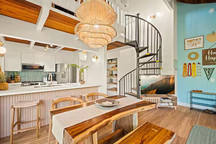 Kitchen open to the living room under a wood ceiling, live-edge table and spiral stair beyond