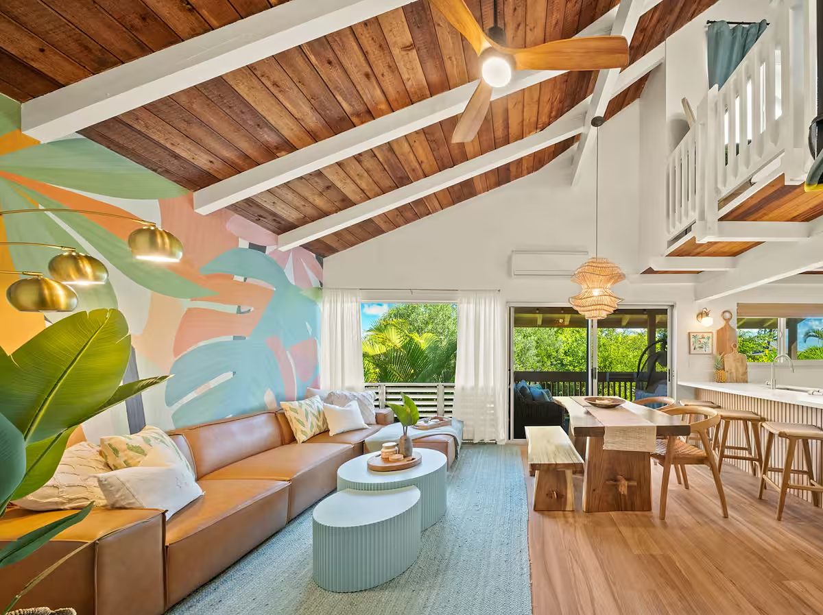 Condo living room with a natural wood ceiling, white beams, a tropical mural and a spiral stair to the loft